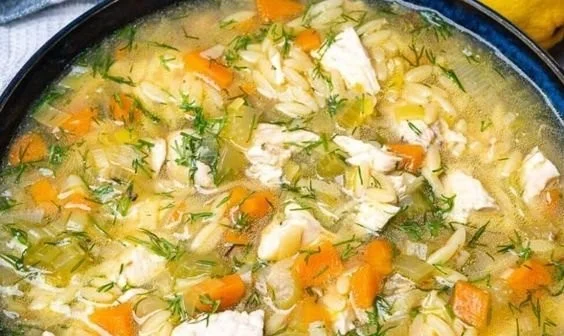 Bowl of Lemon Chicken Orzo Soup garnished with herbs and lemon slices.